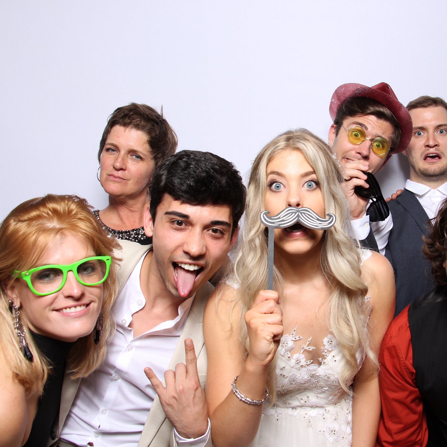 A bride and her friends pose in a wedding photo booth with silly props