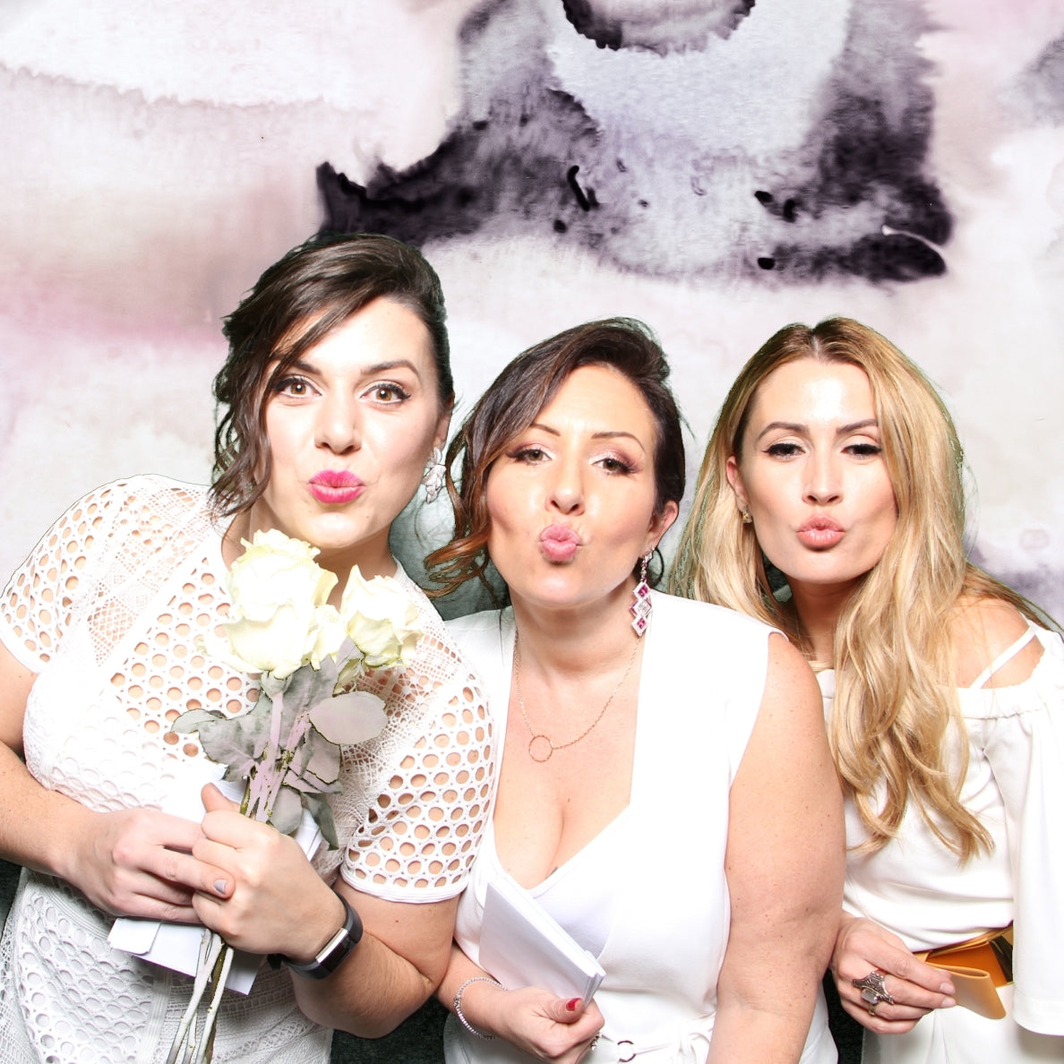 Three bridesmaids posing in a photo booth with flowers