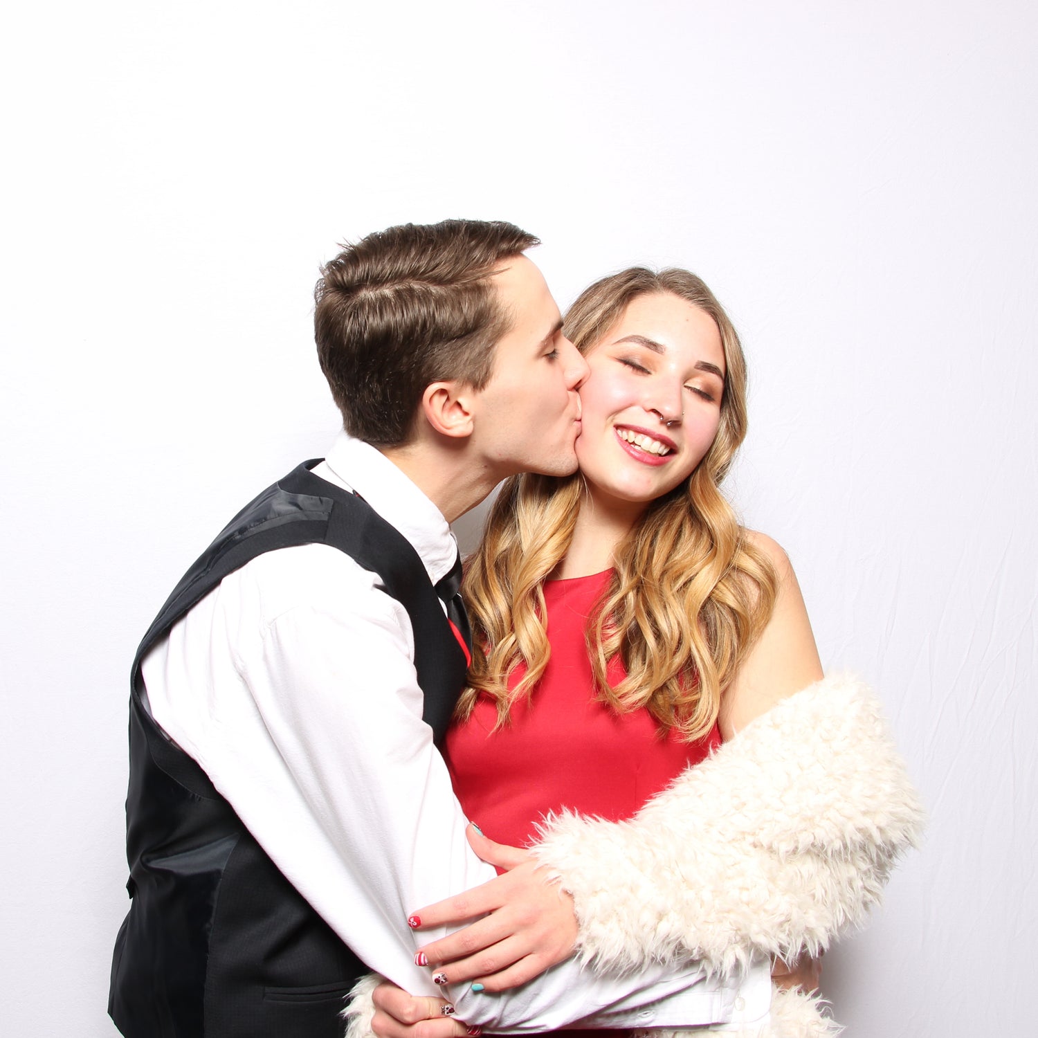 Man in a tuxedo kissing a woman in a red dress in a photo booth