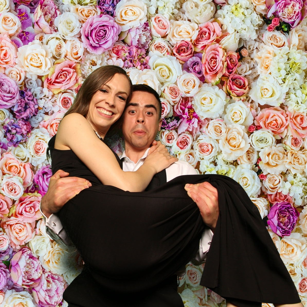 Guy lifting up his girlfriend for a photo booth picture with a flower wall backdrop