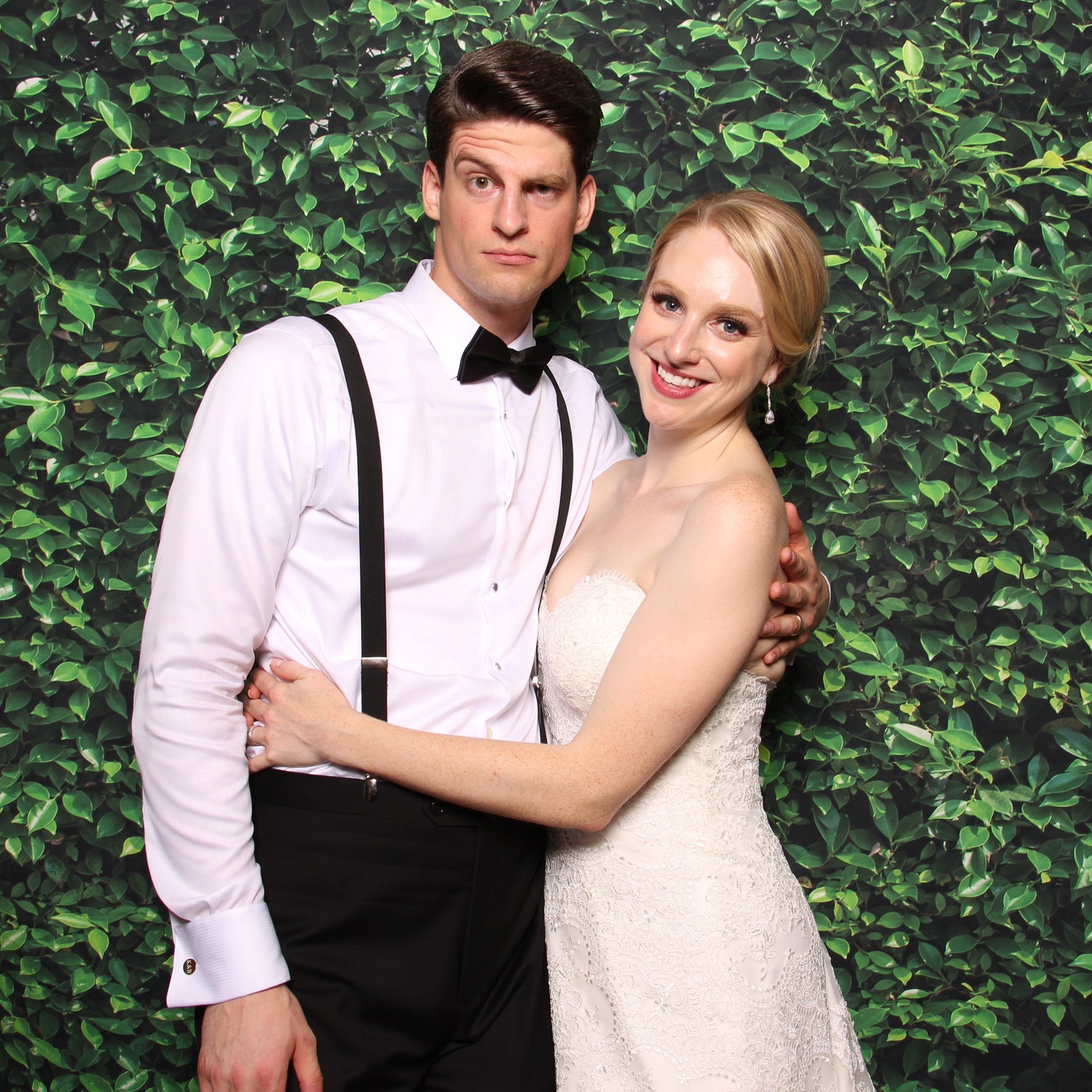 Wedding couple holding each other and posing in front of green leafy backdrop
