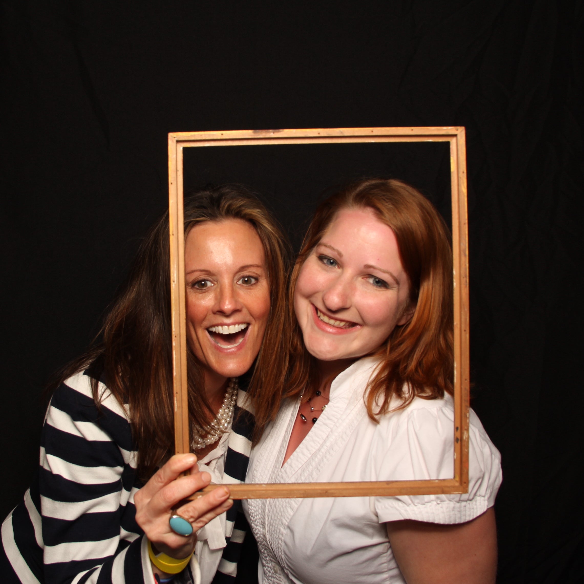 Women posing using a frame as a prop in a photobooth with a black background