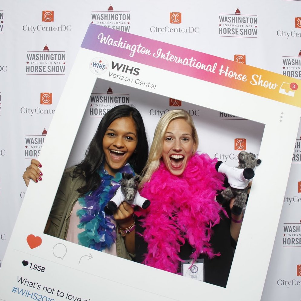 Women in a photo booth at the Washington International Horse Show with a giant Instagram frame prop