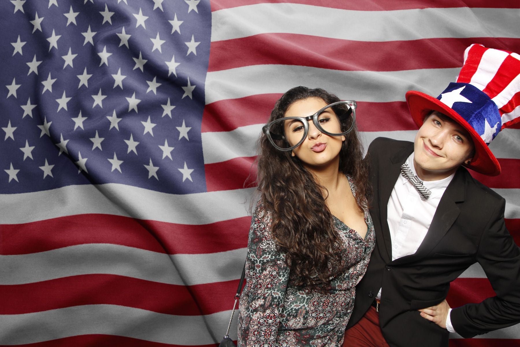 Patriotic couple posing in a photo booth with a USA flag background